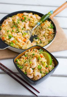 two pans filled with shrimp and rice next to chopsticks on a table