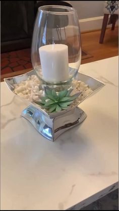 a white candle is sitting in a glass bowl with rocks and succulents