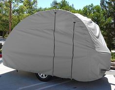 a car covered with a cover parked in a parking lot next to trees and bushes