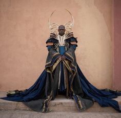 a man dressed in costume sitting on the steps with his hands behind his back and two horns above his head