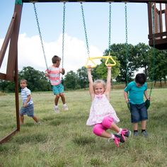 three children playing on a swing set in the grass with their hands up and one child holding