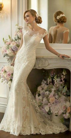 a woman standing next to a fireplace in a white dress with flowers on the mantle