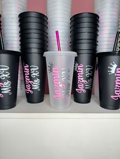 black cups with pink lettering and straws are lined up on a shelf next to each other