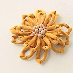 a yellow flower brooch with pearls in the center on a white surface, close up