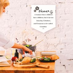 a woman preparing food on top of a wooden table next to a white brick wall