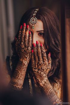 a woman holding her hands to her face while wearing henna and jewelry on her head