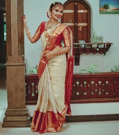 a woman in a red and white sari standing next to a pillar with her hand on