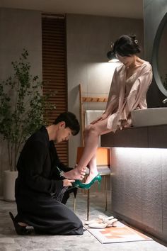 a man kneeling down next to a woman on top of a bathroom counter in front of a mirror