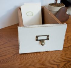 a wooden drawer with a metal handle on top of it next to a potted plant