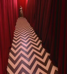 a person standing in the middle of a room with red curtains and black and white chevron floor