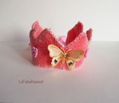 a small pink crown with a butterfly on the front and back side, sitting on a white surface