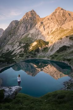 a woman standing on top of a mountain next to a lake in the middle of mountains