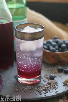 a glass filled with liquid sitting on top of a wooden table next to blueberries