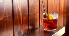 a glass filled with liquid sitting on top of a wooden shelf next to a wall