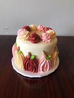 a white cake with pink, yellow and red frosting on a wooden table next to a wall