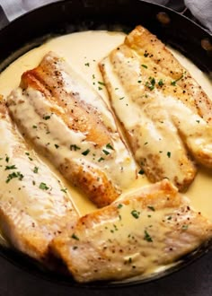 fish covered in gravy sitting in a skillet on a table next to a napkin