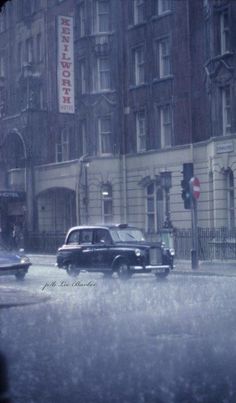 an old black car driving down a street in the rain