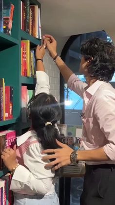 two people reaching for books on a book shelf