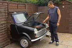 a man standing next to a small car with the hood open and grilling on it