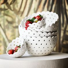 three white bowls filled with strawberries on top of a table next to a wall