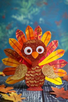 a paper turkey with eyes on it's head, sitting in front of fall leaves