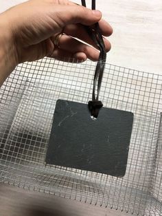 a hand holding a piece of black wire with a square tag attached to the end