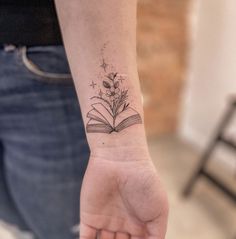 a small tattoo on the wrist of a woman with a book and flowers in it