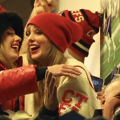 two women in red and white hats are hugging each other at a sporting event with people looking on