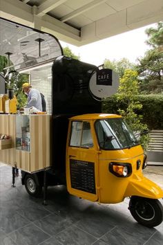 a small yellow truck parked in front of a building with a man standing next to it