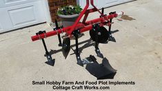 a small red farm and food plot implementr in front of a garage with potted plants