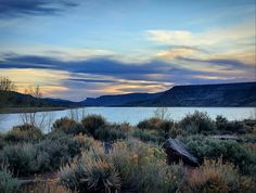 a lake with mountains in the background and clouds in the sky above it at sunset