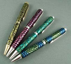 four pens are lined up in a row on a gray surface, one is green and the other is purple