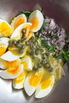 an image of boiled eggs and olives in a bowl with herbs on the side