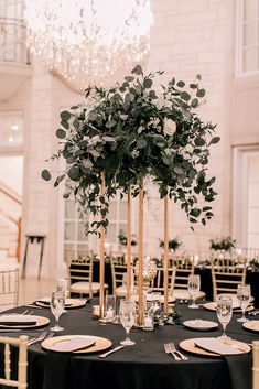 an elegant table setting with black linens and greenery in tall gold candlesticks