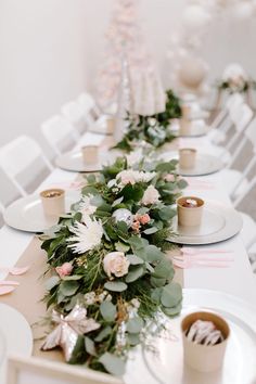 the table is set with white and pink flowers, greenery and candles on it