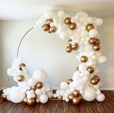 a balloon arch with gold and white balloons in the shape of an o on a wooden floor