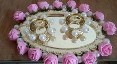 pink roses and pearls on a tray with two gold ring holders in the middle, sitting on a wooden table