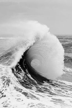 a large wave crashing into the ocean on a cloudy day