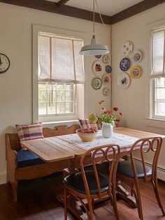 a dining room table with chairs and plates on the wall behind it, along with a bench