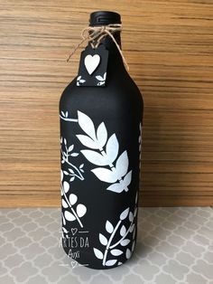 a black bottle with white leaves and hearts on it sitting on top of a table