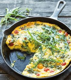 an omelet with tomatoes and greens in a skillet on a wooden table