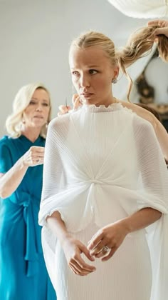 a woman in a white dress getting her hair styled by another woman with blonde hair