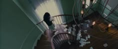 a woman standing on top of a wooden staircase next to a spiral stair case filled with papers