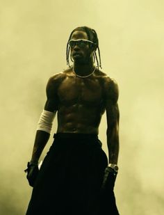 a man with dreadlocks and no shirt standing in front of a foggy sky