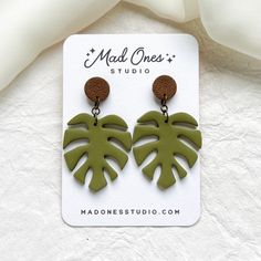 a pair of green and brown leaf earrings on top of a white card with the words mad ones studio