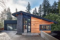 a modern house in the woods with wood siding and stone accents on the front door