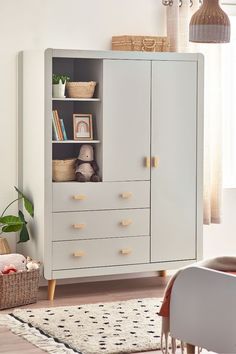 a white cabinet with drawers and baskets on the top shelf next to a rug in a living room