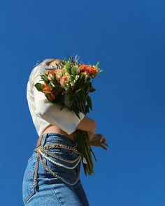 a woman holding flowers up in the air with her back to the camera, against a blue sky