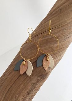 the earrings are made with two different colored leather discs and gold hoops, on top of a piece of wood