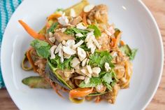 a white plate topped with noodles and vegetables on top of a wooden table next to a blue towel